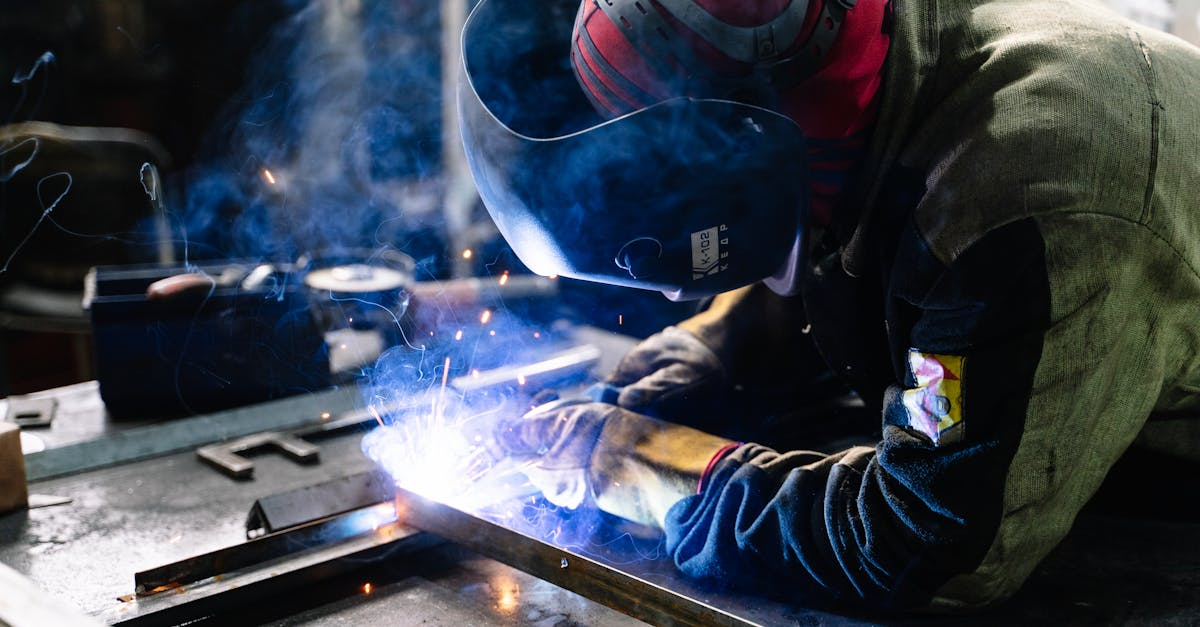A welder works on metal fabrication indoors, creating bright sparks and smoke.